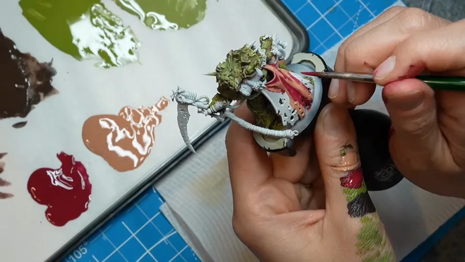 Her wet palette with olive, brown and pink paint while she works on the miniature, Episode 03