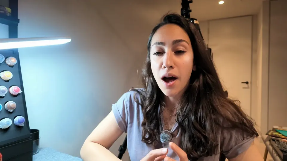 The Pigmentum at her desk talking to camera with the miniature and paints in front of her, Episode 06