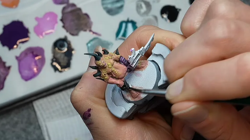 A Poxwalker with black horns on the painting handle, mid edge-highlight, with the purple and grey-blue mixes on the wet palette behind, Episode 05